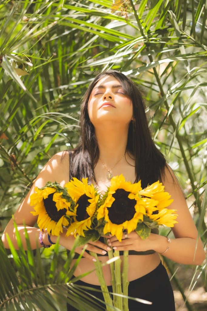 Young woman with sunflowers enjoying sunlight in a lush garden.